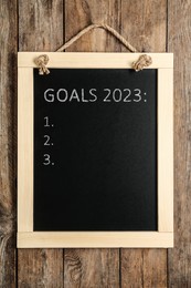 Blackboard with phrase GOALS 2023 and empty checklist on hanging on wooden background