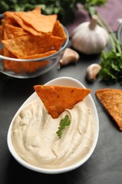 Delicious hummus with nacho chip and parsley on black table, closeup