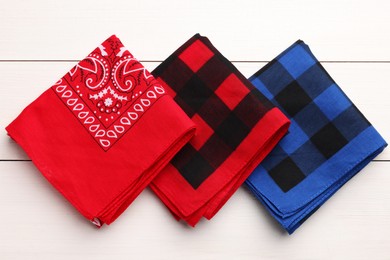 Photo of Folded bandanas with different patterns on white wooden table, flat lay