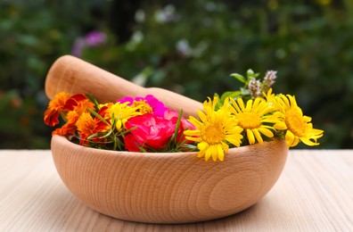 Mortar with pestle and beautiful fresh flowers on wooden table outdoors
