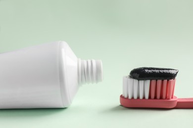 Photo of Brush and tube with charcoal toothpaste on white background, closeup