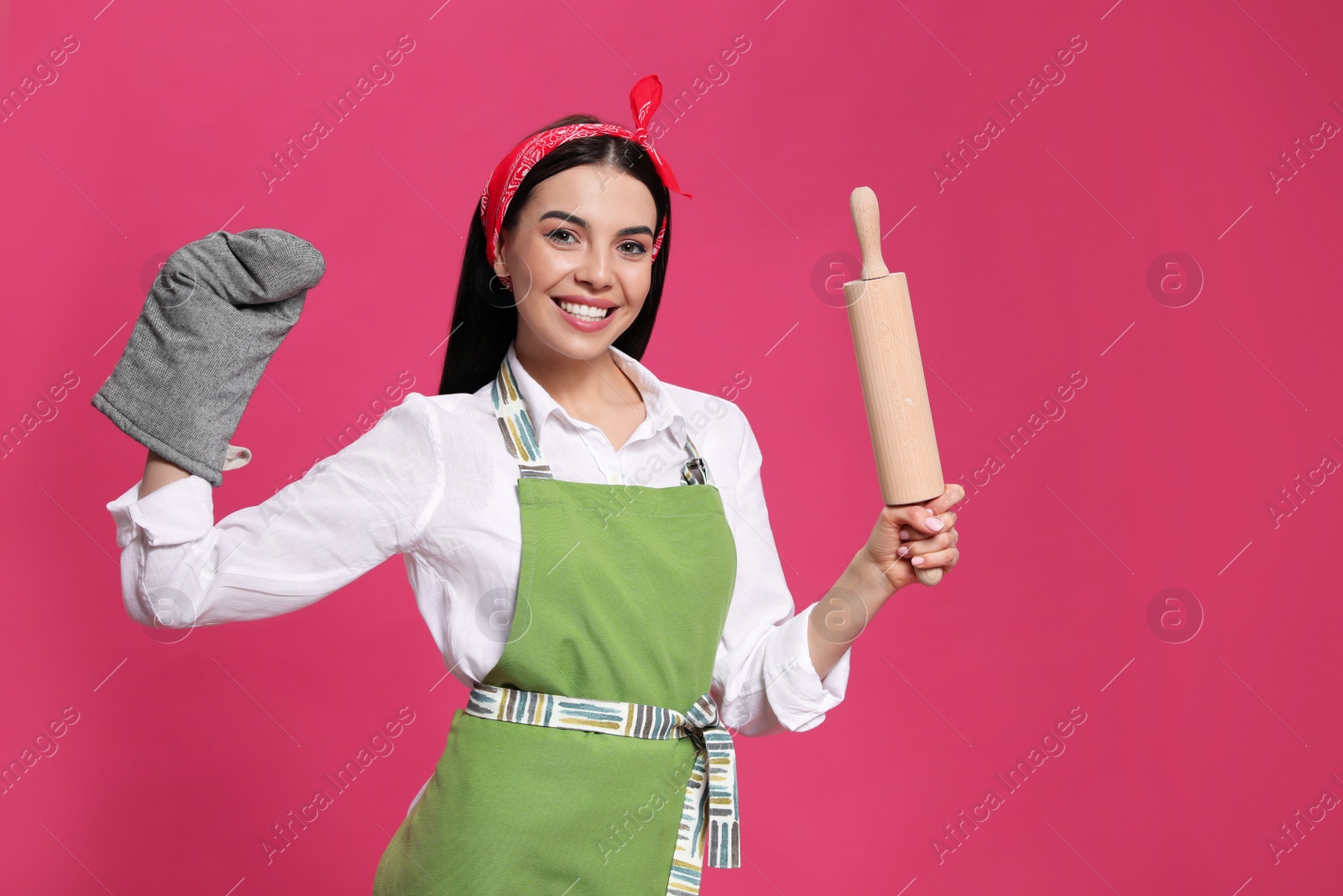 Photo of Young housewife in oven glove holding rolling pin on pink background. Space for text