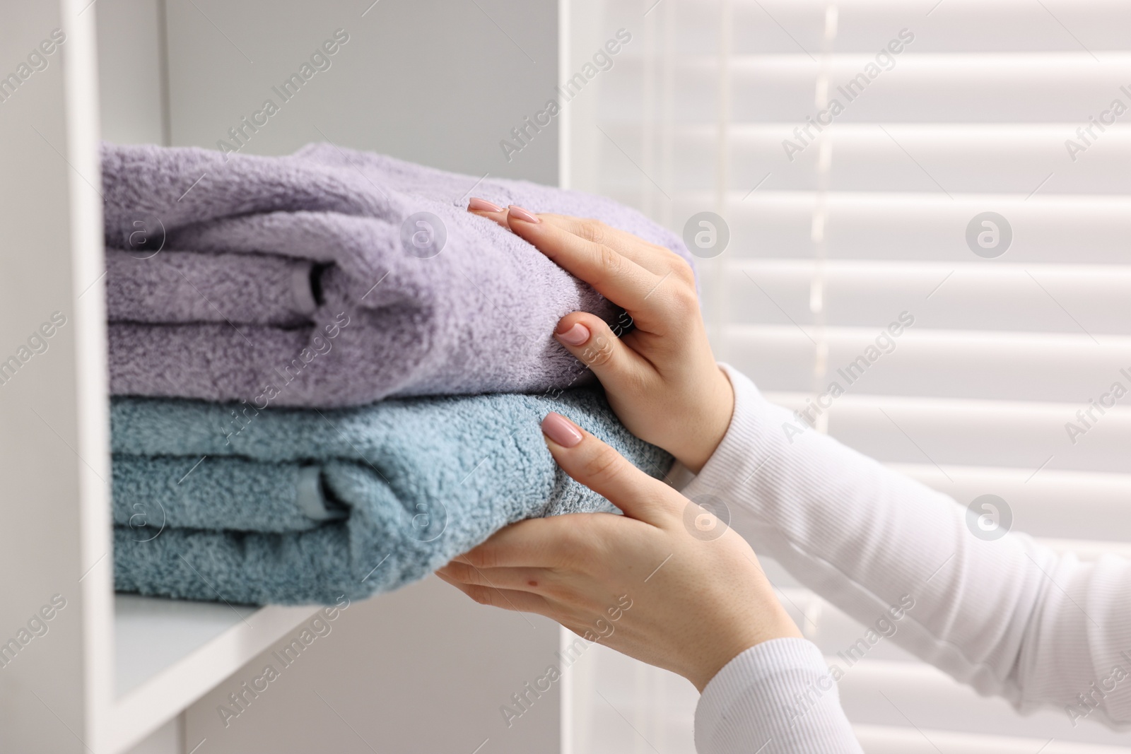 Photo of Woman stacking clean towels on shelf indoors, closeup