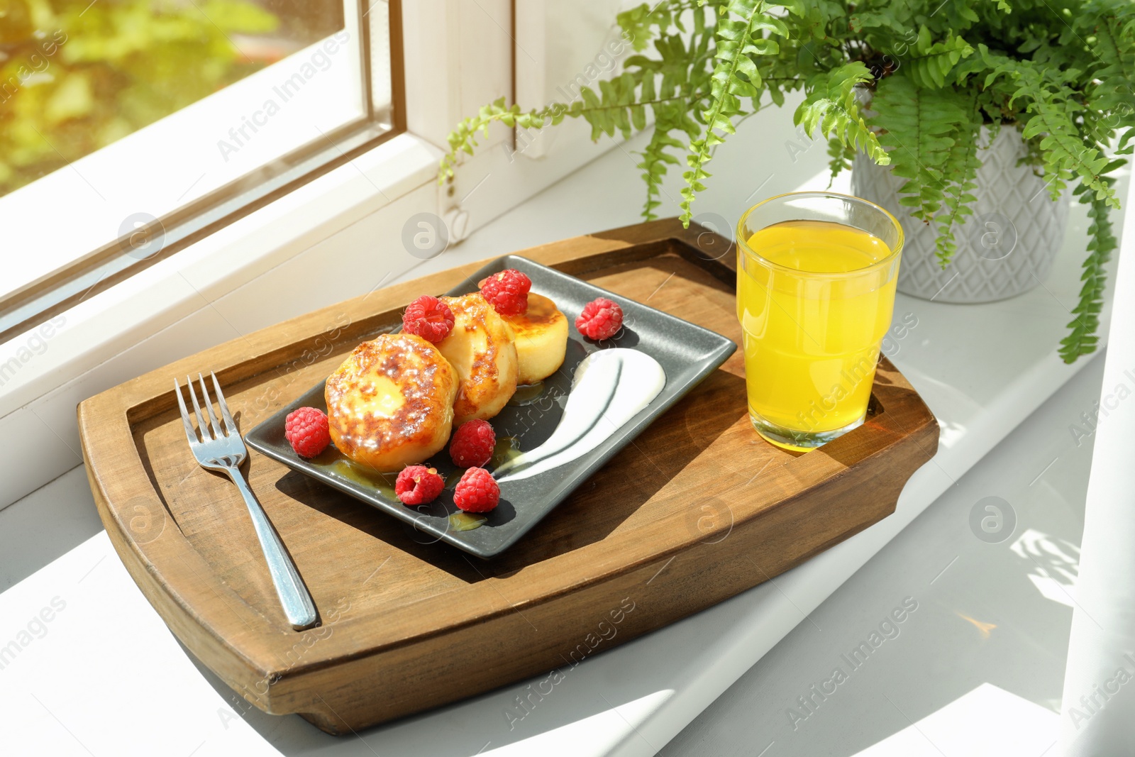 Photo of Cottage cheese pancakes with fresh raspberries and sour cream on wooden tray near window