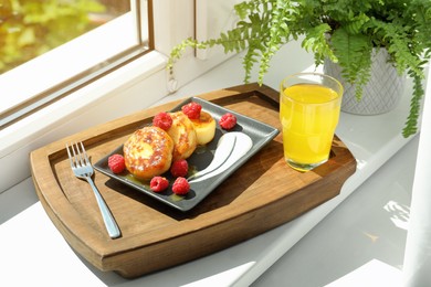 Cottage cheese pancakes with fresh raspberries and sour cream on wooden tray near window