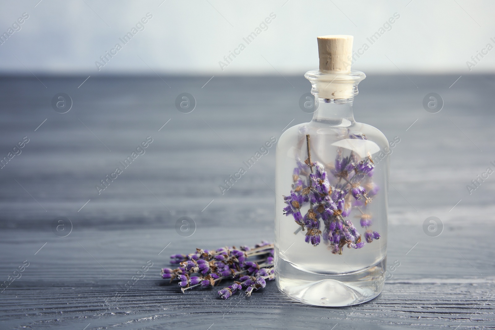 Photo of Natural herbal oil and lavender flowers on wooden table. Space for text