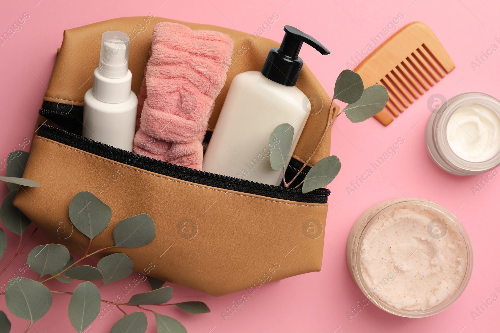 Photo of Preparation for spa. Compact toiletry bag with different cosmetic products, comb and eucalyptus on pink background, flat lay