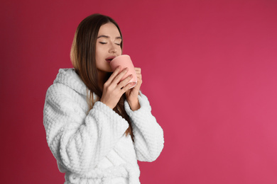 Photo of Young woman in bathrobe with cup of morning drink on crimson background, space for text