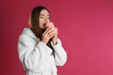 Young woman in bathrobe with cup of morning drink on crimson background, space for text