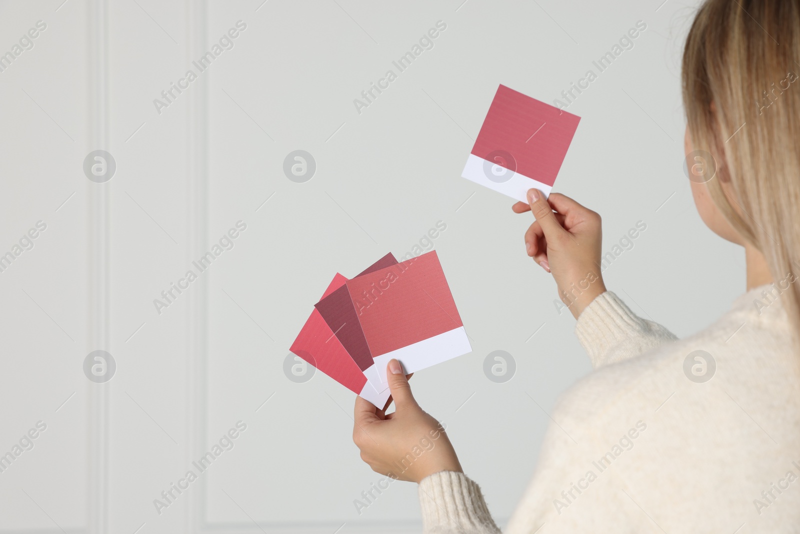 Photo of Woman choosing paint shade for wall indoors, focus on hands with color sample cards. Interior design