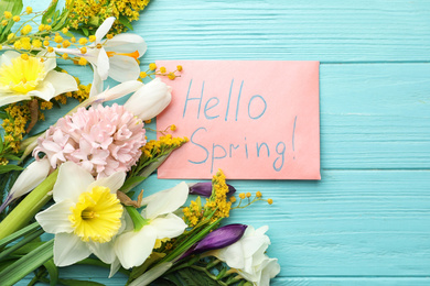 Pink card with words HELLO SPRING and fresh flowers on light blue wooden table, flat lay