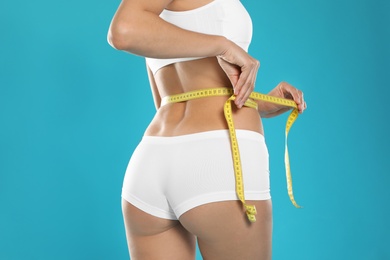 Photo of Slim young woman with smooth gentle skin in underwear measuring body on color background, closeup