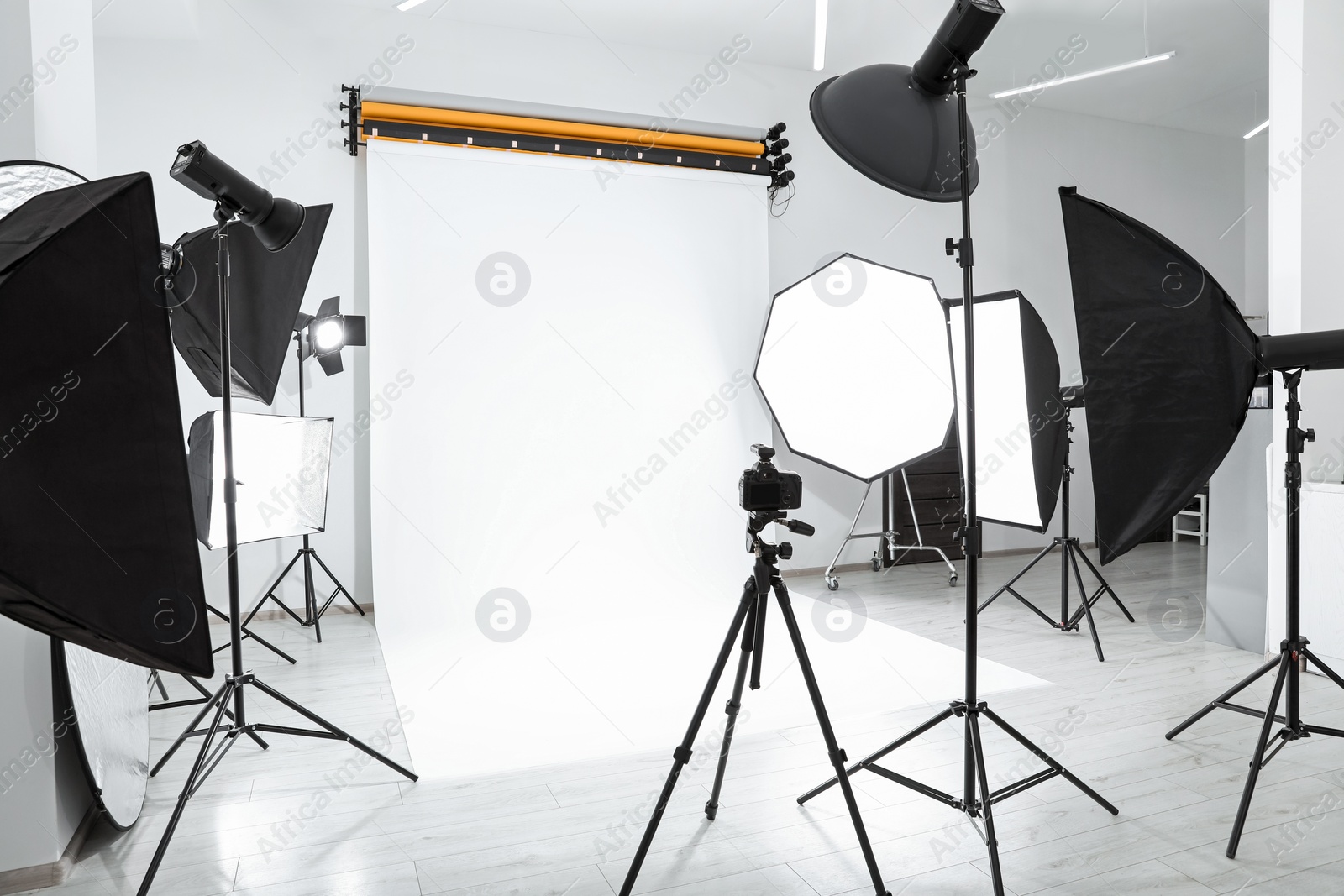 Photo of Tripod with camera and professional lighting equipment in modern photo studio