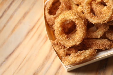 Cardboard box with crunchy fried onion rings on wooden background, closeup. Space for text