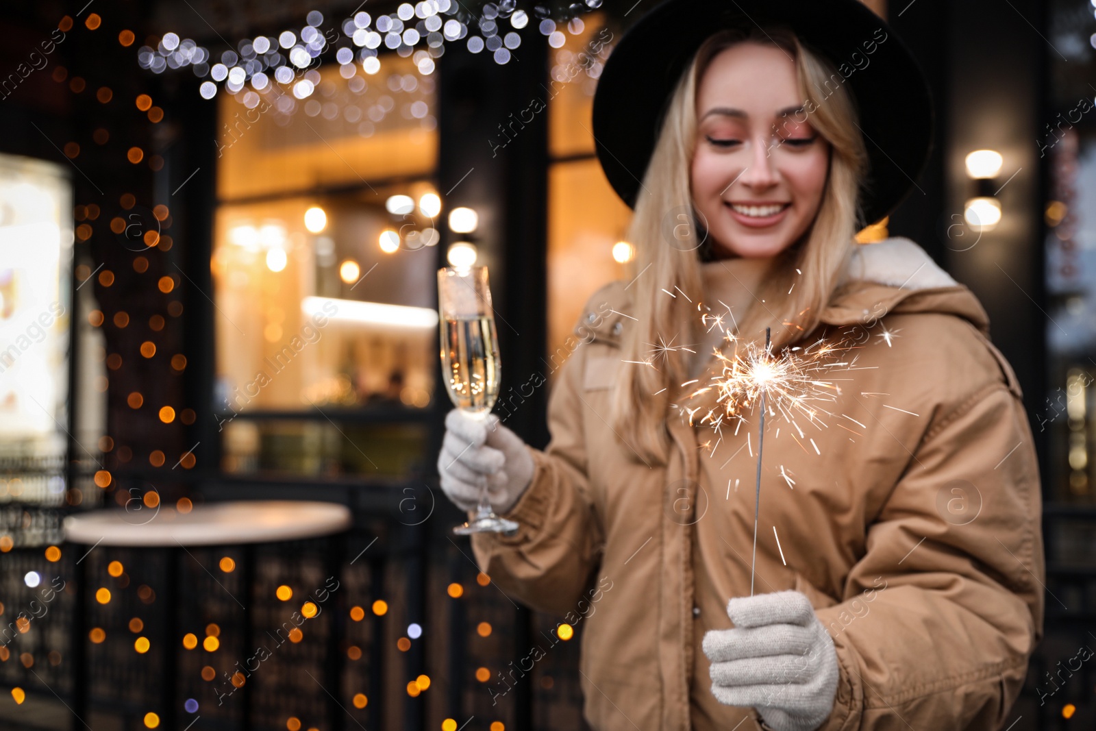 Photo of Happy young woman with sparkler and glass of champagne at winter fair