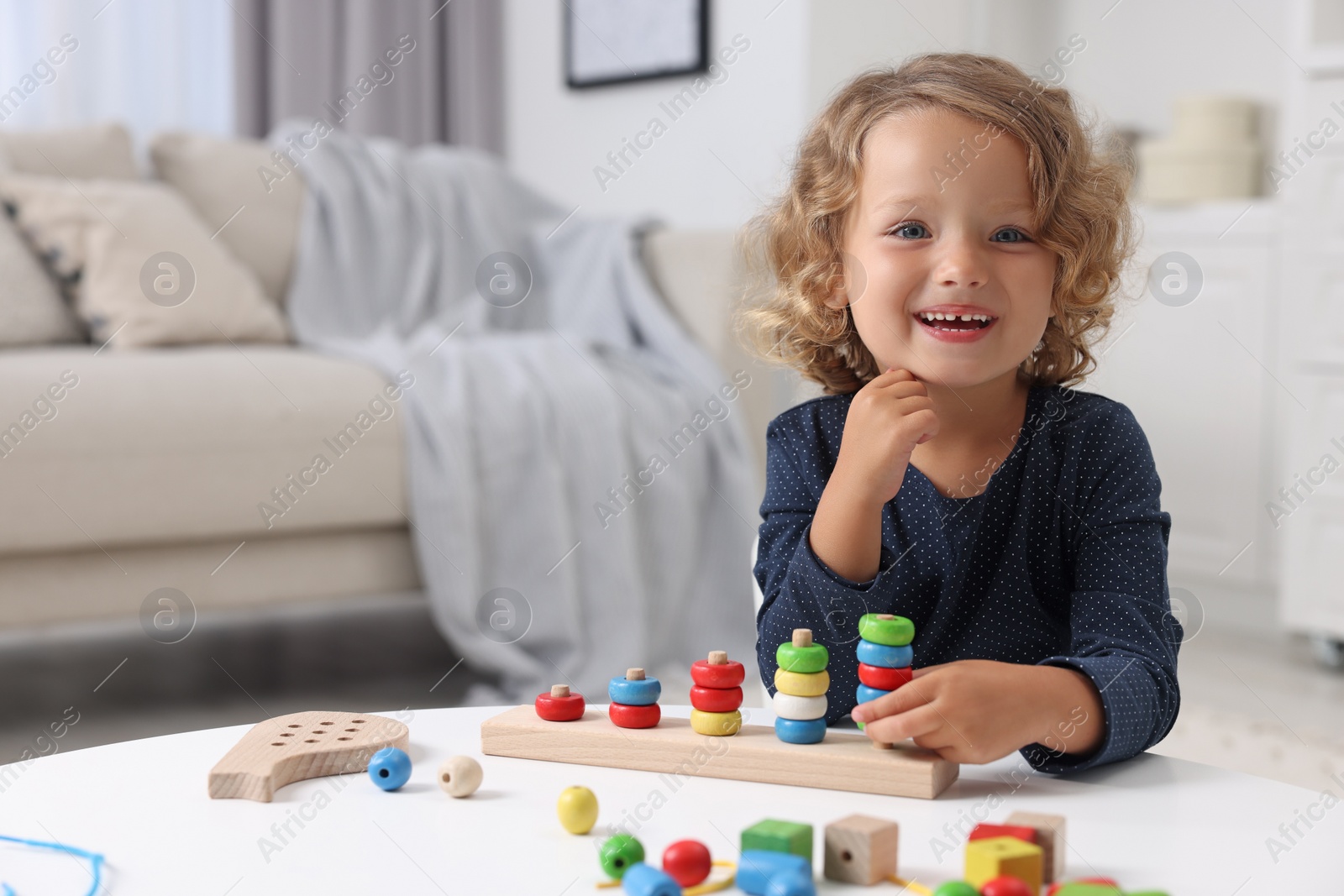 Photo of Motor skills development. Little girl playing with stacking and counting game at table indoors