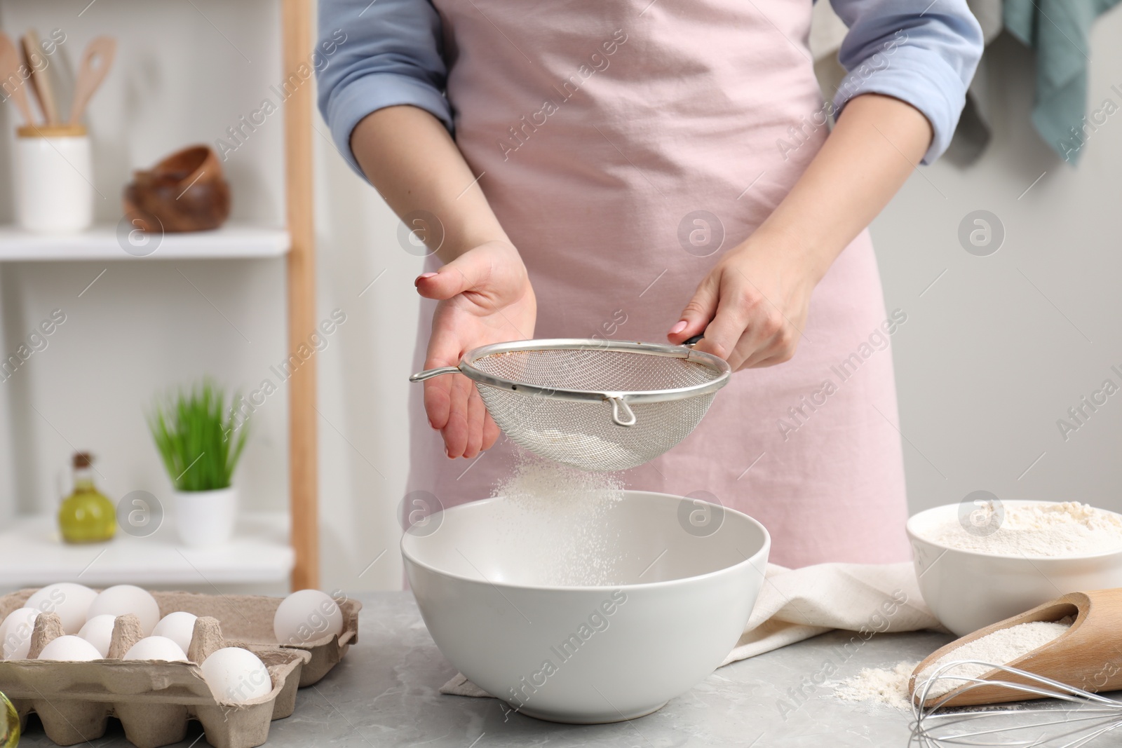 Photo of Making tasty baklava. Woman sifting flour into bowl at light grey marble table, closeup