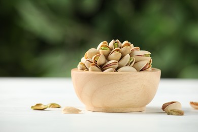 Tasty pistachios in bowl on white wooden table against blurred background, closeup. Space for text