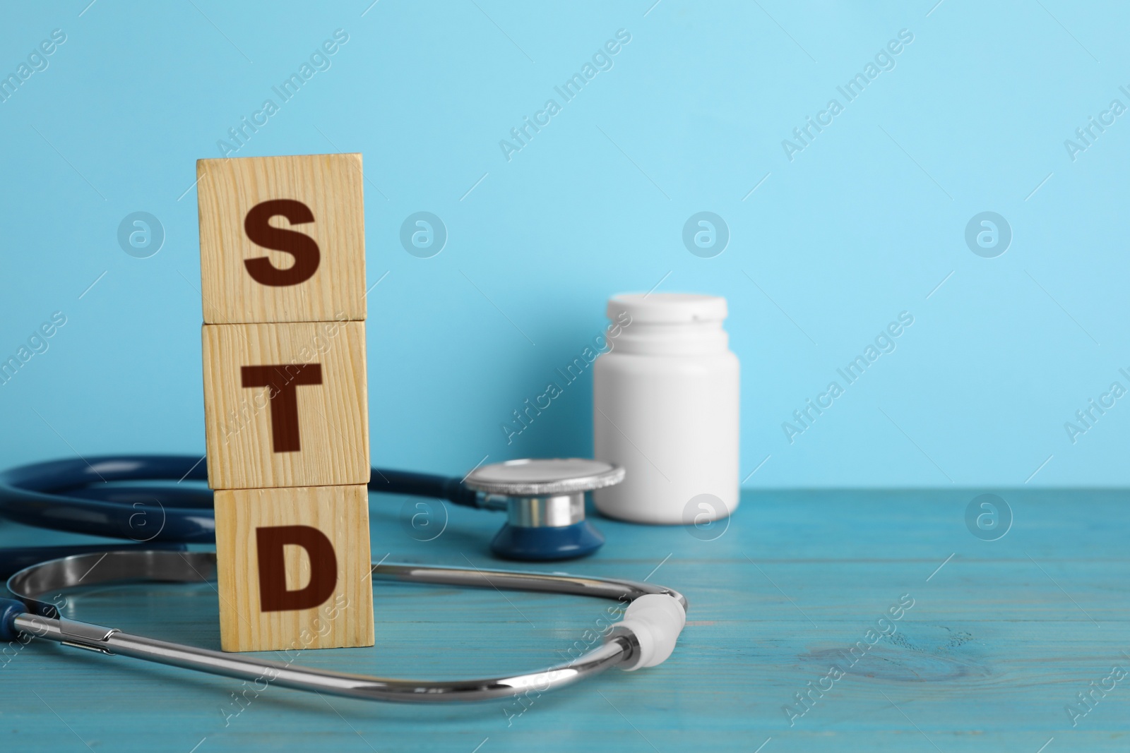 Photo of Abbreviation STD made with cubes and stethoscope on light blue wooden table, space for text