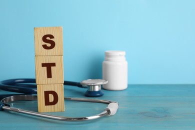 Photo of Abbreviation STD made with cubes and stethoscope on light blue wooden table, space for text