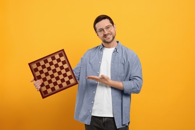 Photo of Smiling man pointing at chessboard on orange background