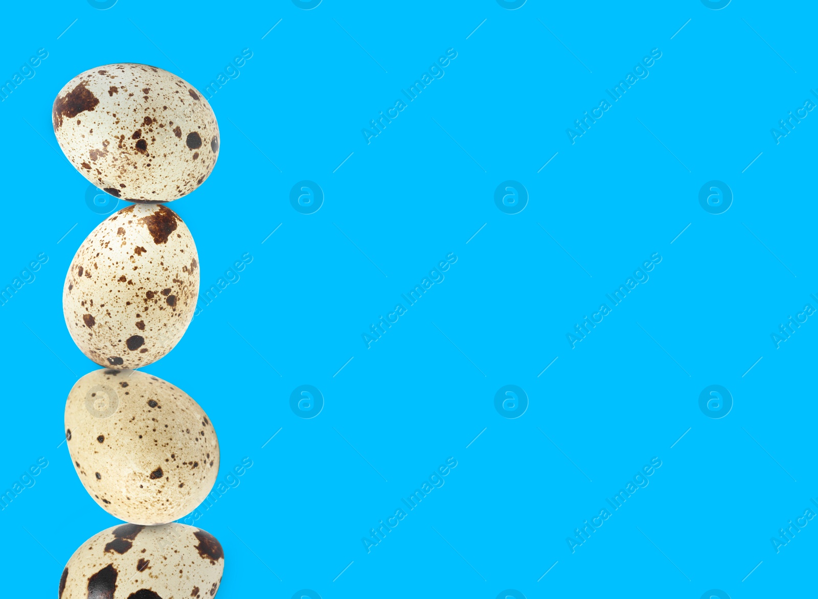 Image of Stacked speckled quail eggs on light blue background. Space for text