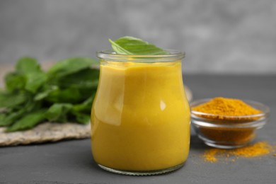 Photo of Tasty curry sauce, powder and basil leaves on grey table