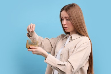 Photo of Emotional woman untangling her lost hair from comb on light blue background. Alopecia problem
