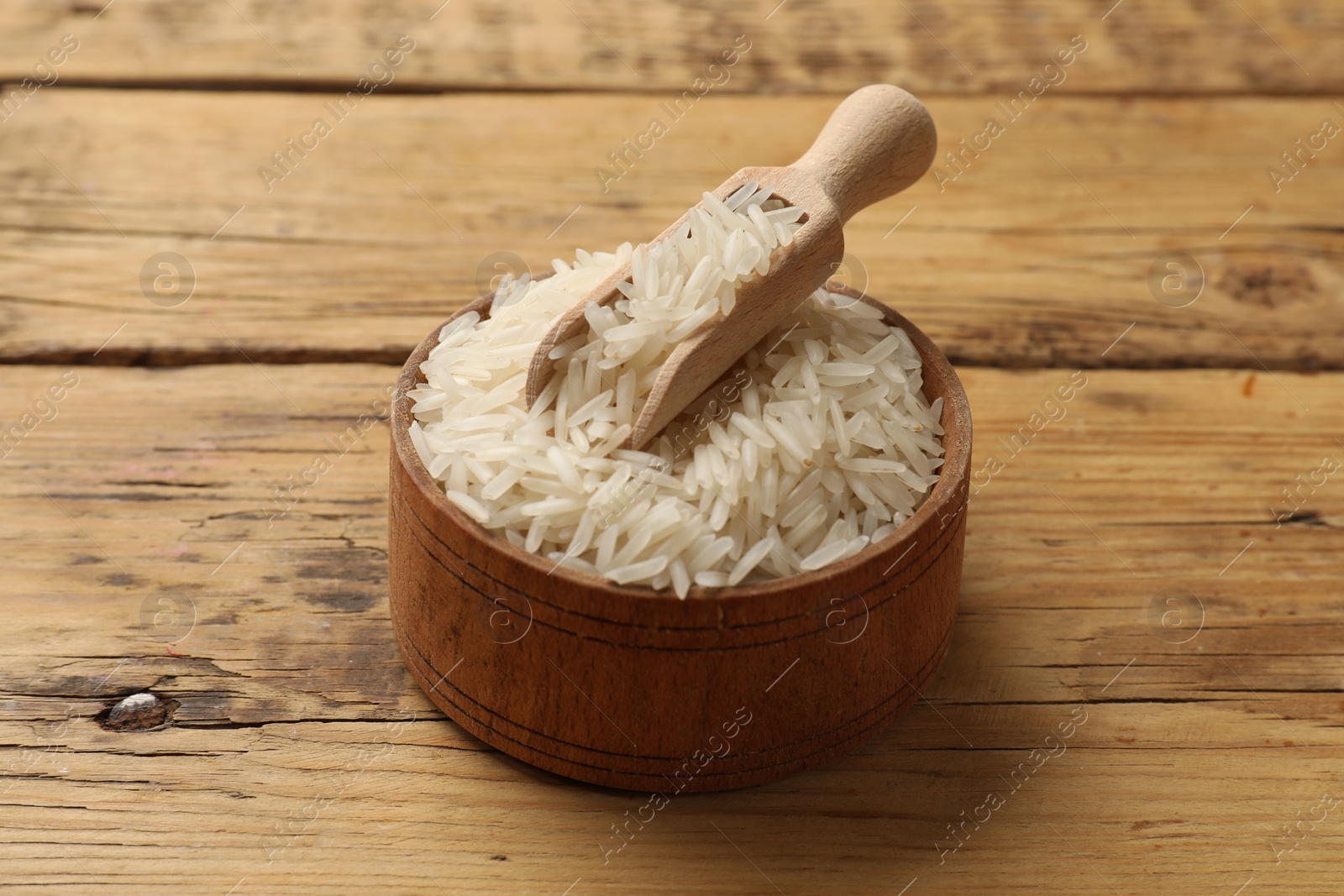 Photo of Raw basmati rice in bowl and scoop on wooden table