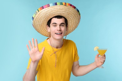 Young man in Mexican sombrero hat with cocktail on light blue background