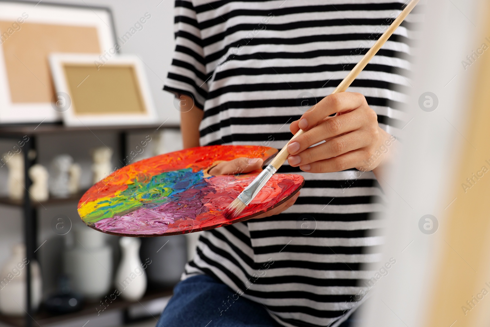 Photo of Young woman mixing paints on palette with brush in studio, closeup