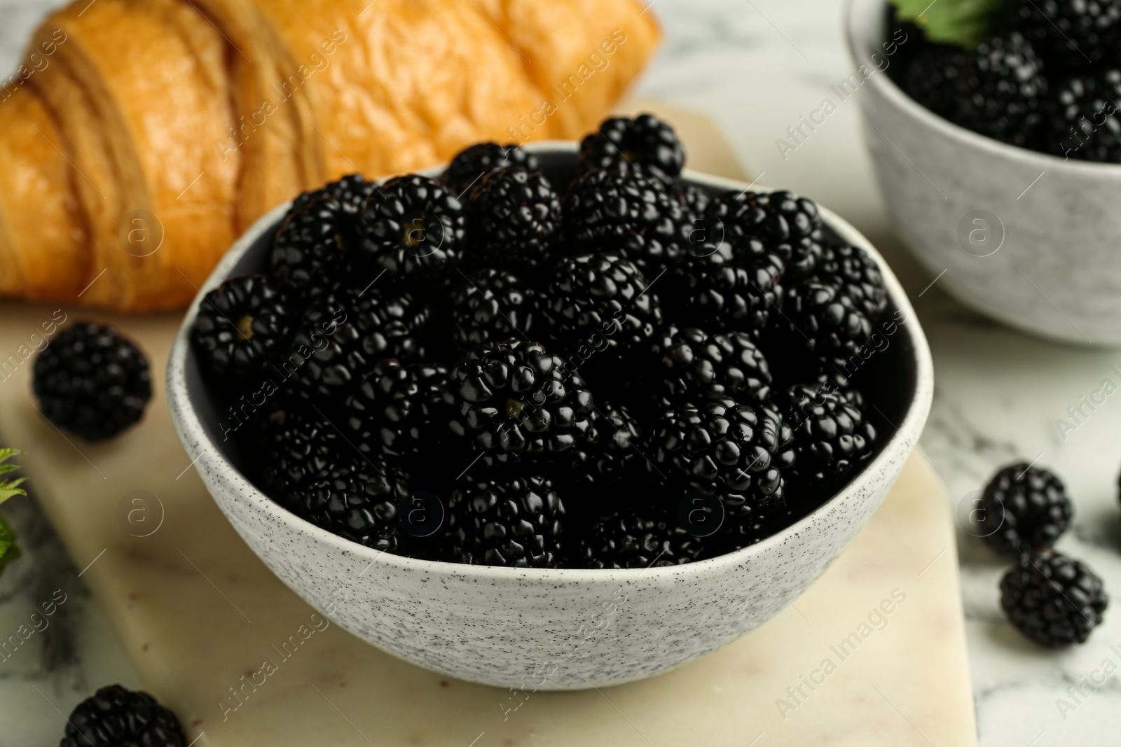 Photo of Bowl of fresh ripe blackberries on white marble table, closeup