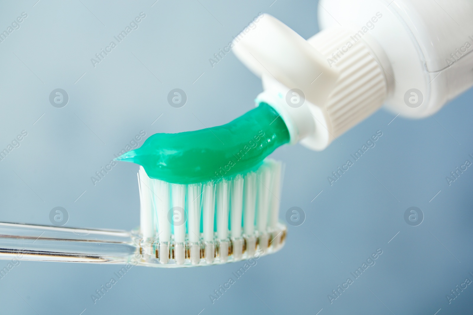 Photo of Squeezing toothpaste on brush against color background, closeup