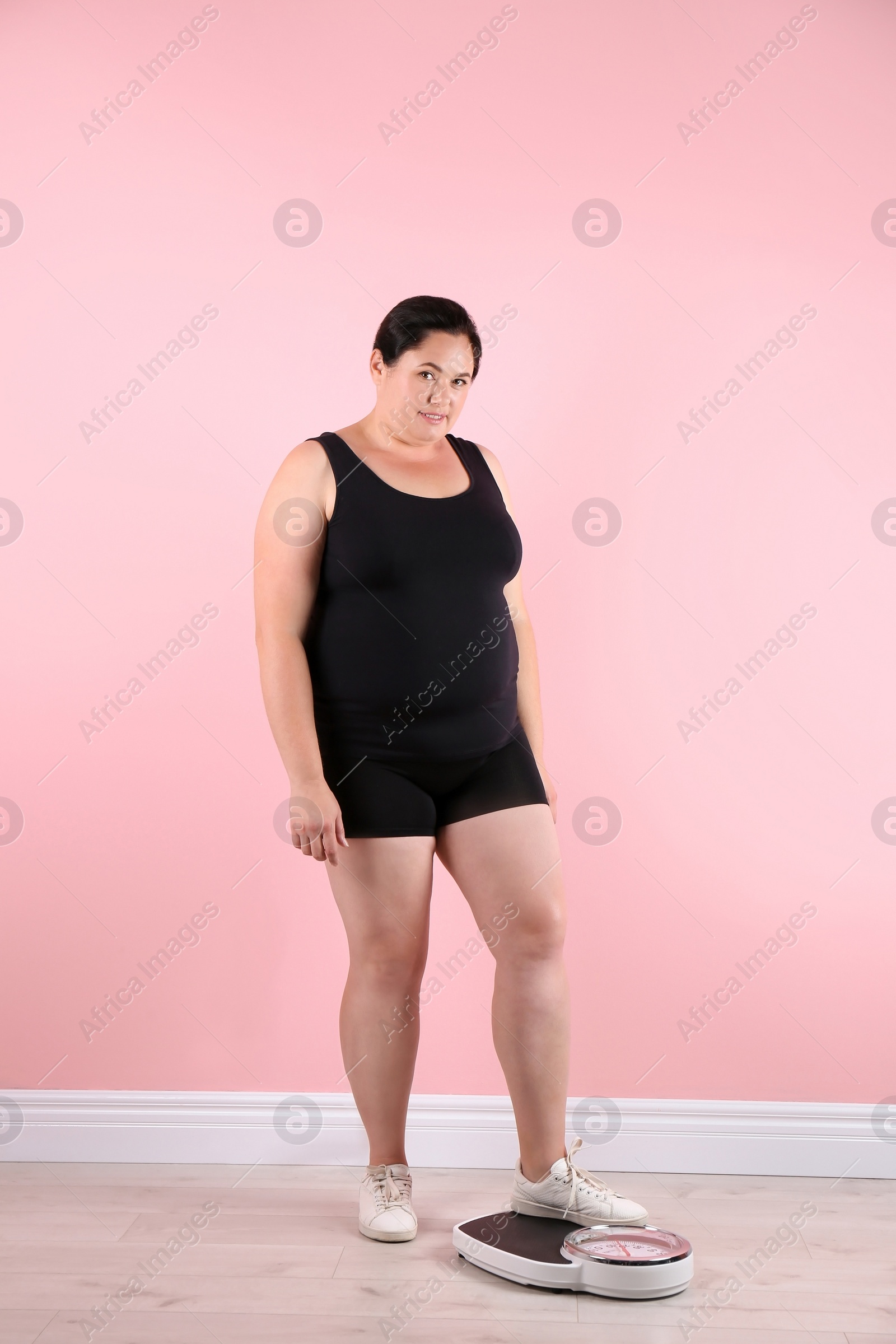 Photo of Overweight woman in sportswear using scales near color wall