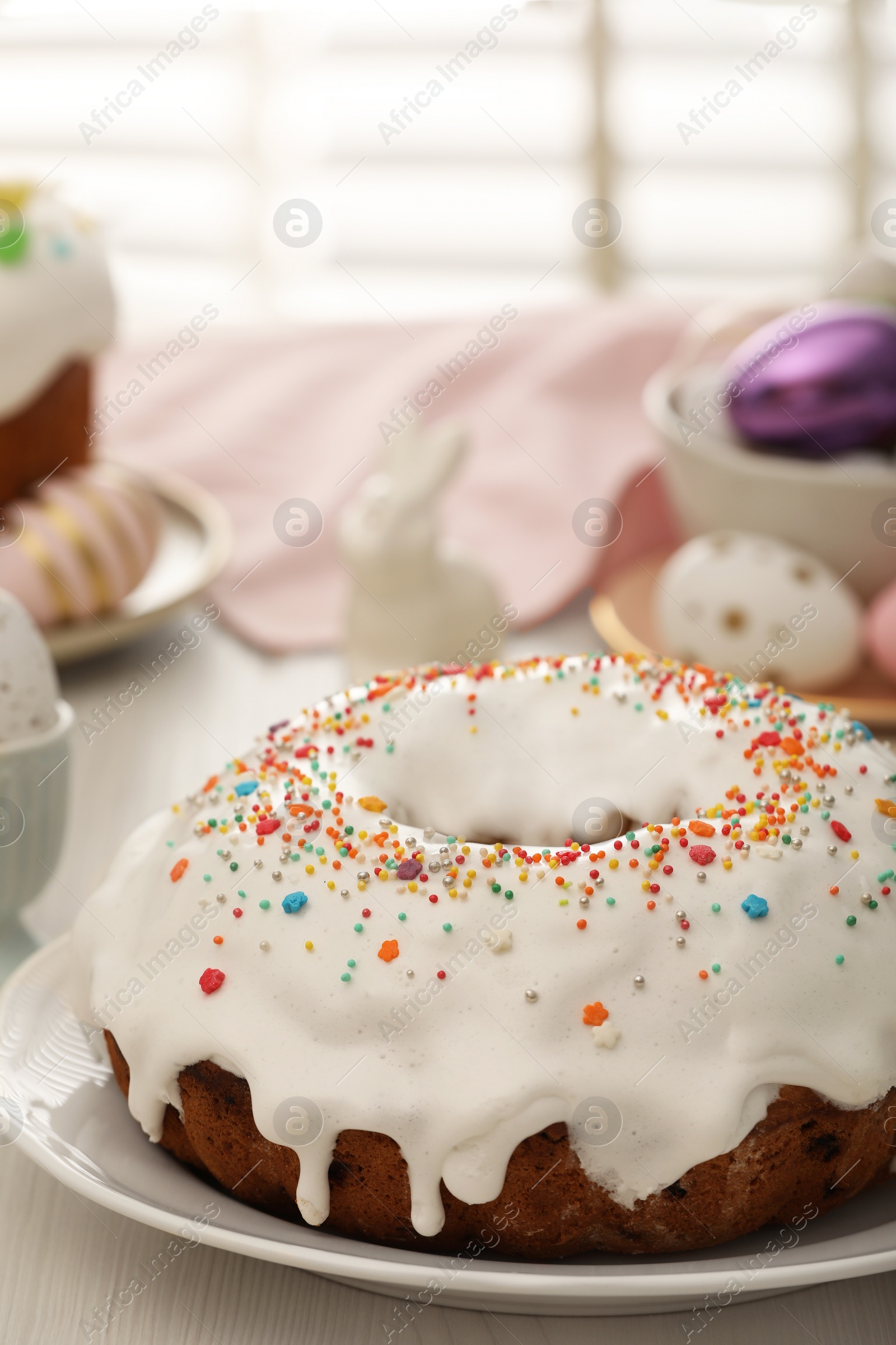 Photo of Delicious Easter cake decorated with sprinkles near painted eggs on white wooden table, closeup