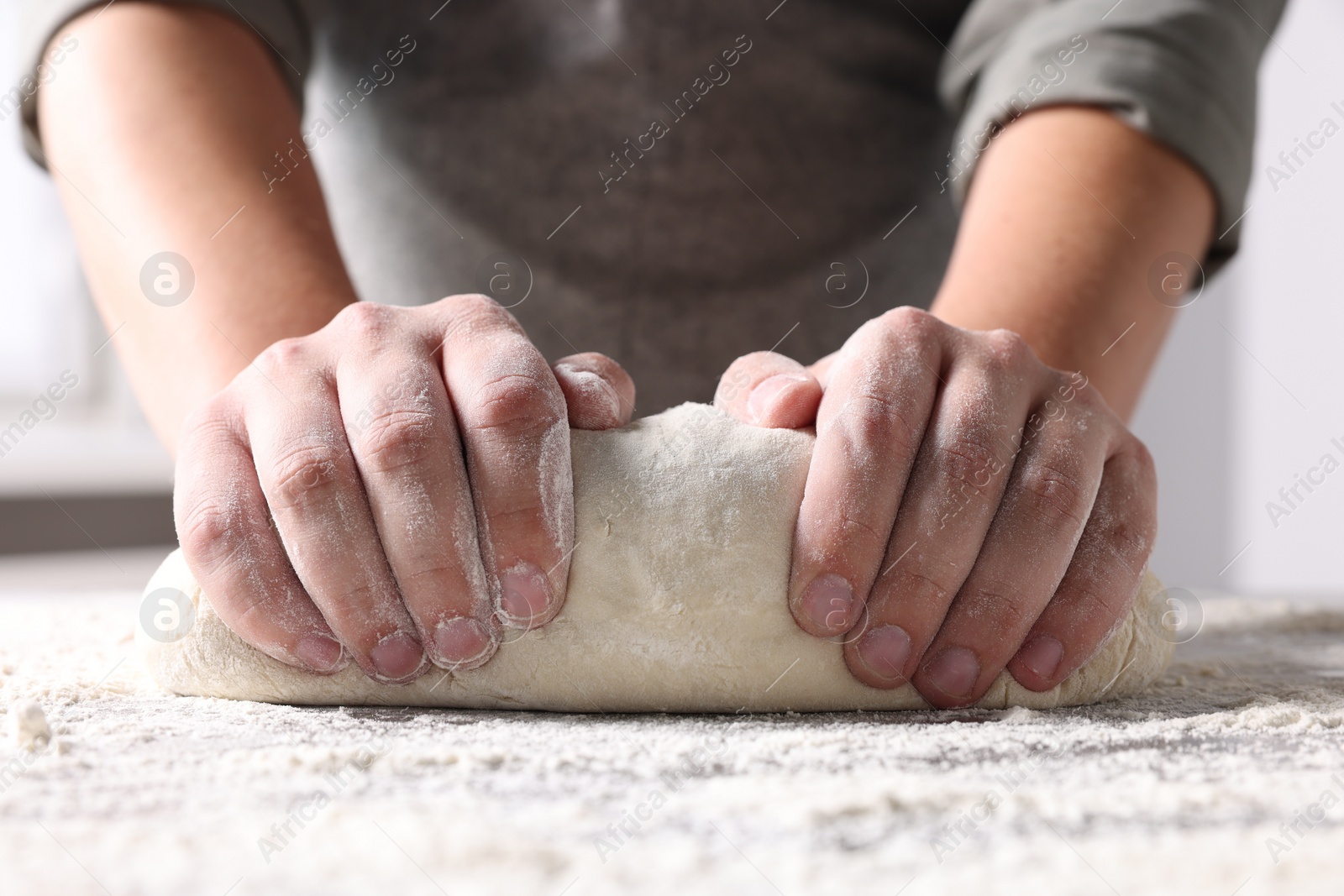 Photo of Man kneading dough at table in kitchen, closeup