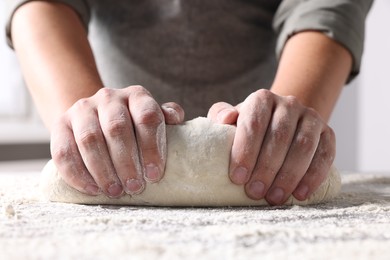 Photo of Man kneading dough at table in kitchen, closeup