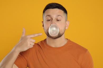 Photo of Handsome man blowing bubble gum on orange background