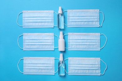 Photo of Hand sanitizers and medical masks on light blue background, flat lay