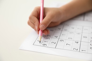 Photo of Little child solving sudoku puzzle at white table, closeup