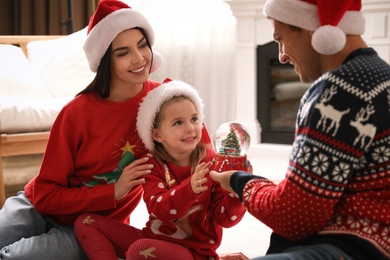 Photo of Family in Santa hats playing with snow globe at home