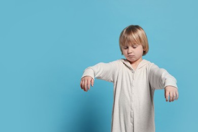 Boy in pajamas sleepwalking on light blue background, space for text