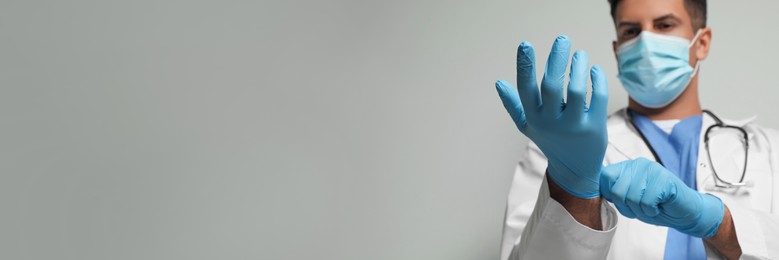 Surgeon putting on medical gloves against light grey background, focus on hands. Banner design with space for text
