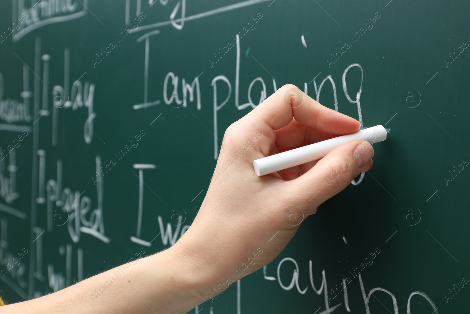 Photo of English teacher writing with chalk on green chalkboard, closeup