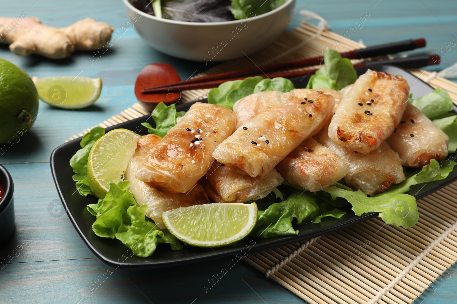 Photo of Tasty fried spring rolls, lettuce and lime on light blue wooden table, closeup