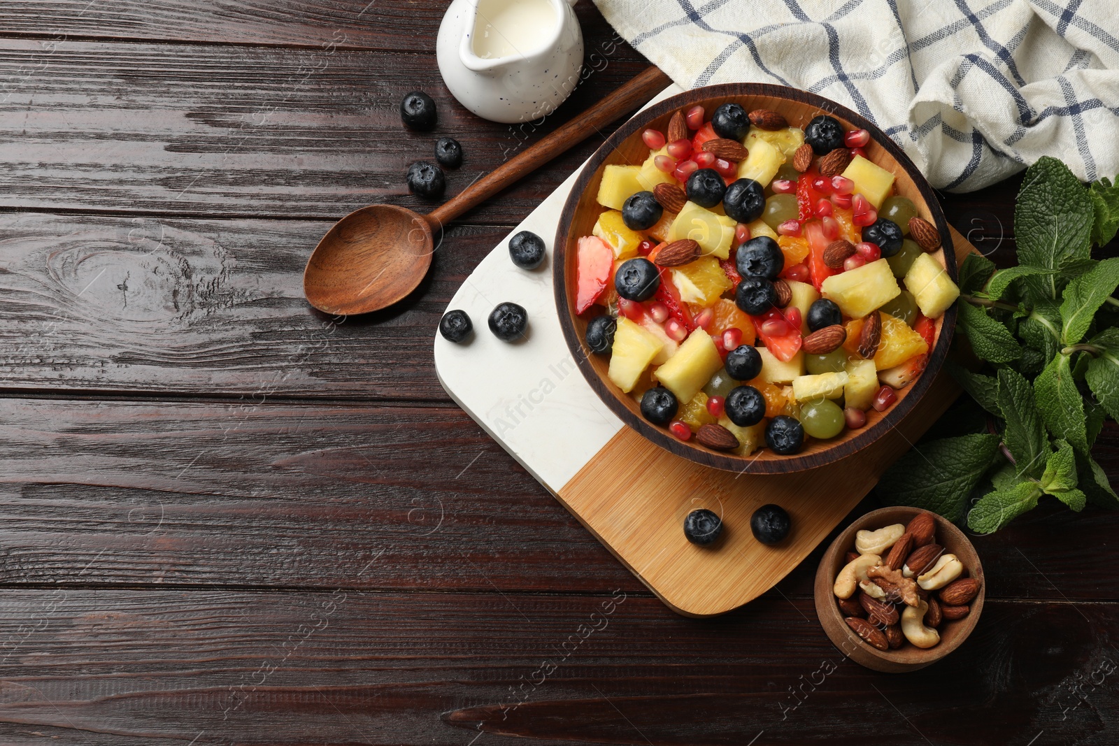 Photo of Delicious fruit salad in bowl, berries, nuts and fresh mint on wooden table, flat lay. Space for text.