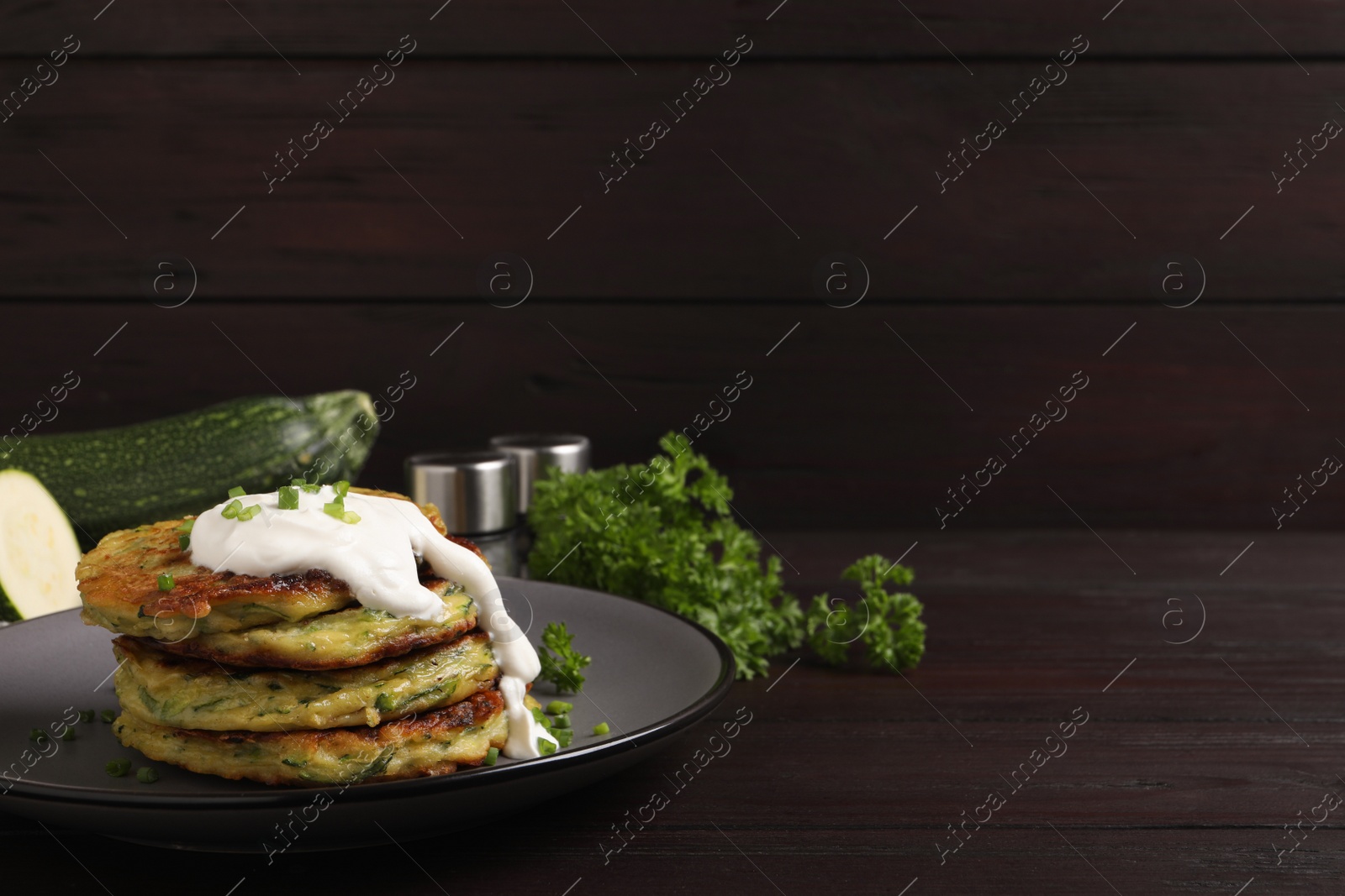 Photo of Delicious zucchini fritters with sour cream on wooden table. Space for text