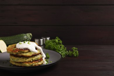 Delicious zucchini fritters with sour cream on wooden table. Space for text