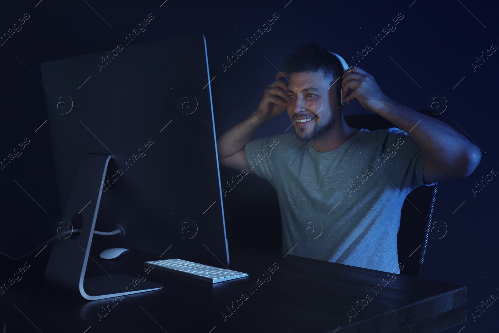 Photo of Happy man with headphones playing video game on modern computer in dark room