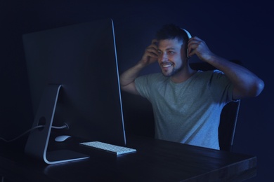 Photo of Happy man with headphones playing video game on modern computer in dark room